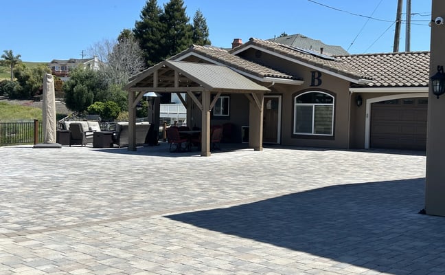 Modern home with covered patio, two-car garage, and paver driveway overlooking hillside landscape